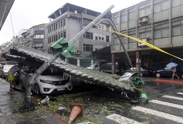 A man looks at a car damaged by fallen roof near a bent traffic light caused by strong winds from Typhoon Soudelor in Taipei