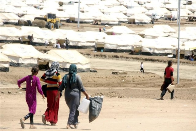 Varias mujeres se dirigen a recoger agua en un campo de refugiados cerca del puesto fronterizo