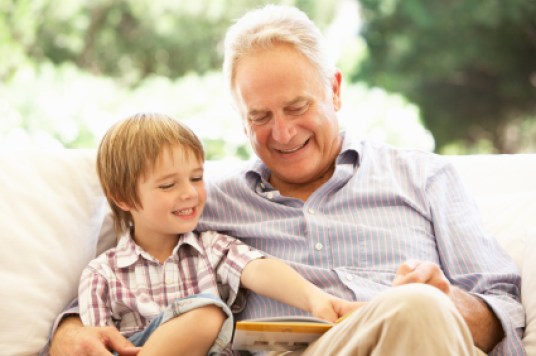 Grandfather With Grandson Reading Together On Sofa