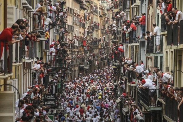 Participants run ahead of Pedraza de Yeltes' fighting bulls on the fourth day of the San Fermin bull run festival in Pamplona, northern Spain on July 10, 2016. On each day of the festival six bulls are released at 8:00 a.m. (0600 GMT) to run from their corral through the narrow, cobbled streets of the old town over an 850-meter (yard) course. Ahead of them are the runners, who try to stay close to the bulls without falling over or being gored. / AFP PHOTO / PEDRO ARMESTRE