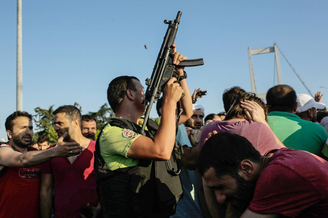 A police officer holds a weapon as people react after they took over military position on the Bosphorus bridge in Istanbul on July 16, 2016. President Recep Tayyip Erdogan battled to regain control over Turkey on July 16, 2016 after a coup bid by discontented soldiers, as signs grew that the most serious challenge to his 13 years of dominant rule was faltering. After a night of drama and bloodshed, at least 90 people had died and more than 1,150 people were wounded, according to state-run news agency Andalou. / AFP PHOTO / Yasin AKGUL