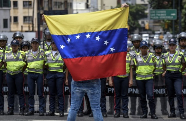 Un miembro de la oposición de la Venezuela representa una bandera nacional frente a policías nacionales durante una manifestación en Caracas el 27 de julio de 2016. La oposición de Venezuela llamó a protestas el miércoles para exigir las autoridades electorales permiten un referéndum sobre la eliminación de presidente, Nicolás Maduro, del poder. AFP PHOTO / JUAN BARRETO