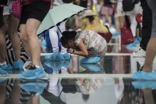 A girl looks through the glass on the world's highest and longest glass-bottomed bridge is seen above a valley in Zhangjiajie in China's Hunan Province on August 20, 2016. / AFP PHOTO / FRED DUFOUR