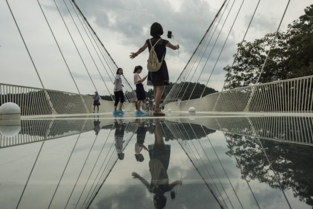 A tourist takes a photograph on the world's highest and longest glass-bottomed bridge above a valley in Zhangjiajie in China's Hunan Province on August 20, 2016. / AFP PHOTO / FRED DUFOUR