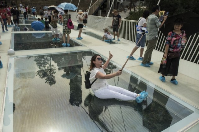 A tourist takes a photograph on the world's highest and longest glass-bottomed bridge above a valley in Zhangjiajie in China's Hunan Province on August 20, 2016. / AFP PHOTO / FRED DUFOUR