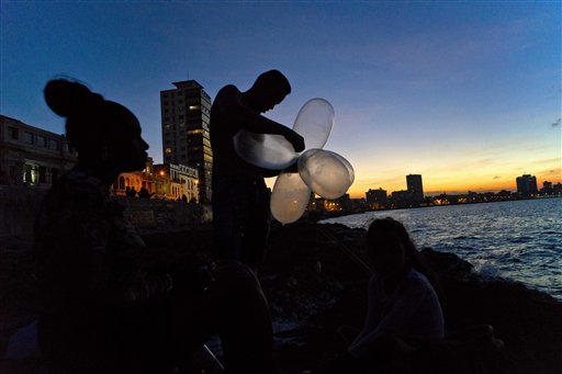 En esta imagen del 13 de noviembre de 2016, el mecánico Junio Torres López infla varios condones para su sedal que mantengan alta la carnada en el agua y aumentar la resistencia de la línea contra el peso de peces pesados, mientras su esposa Edelmis Ferro Solano se sienta cerca en al malecón, al atardecer en La Habana, Cuba. (AP Foto/Ramon Espinosa)