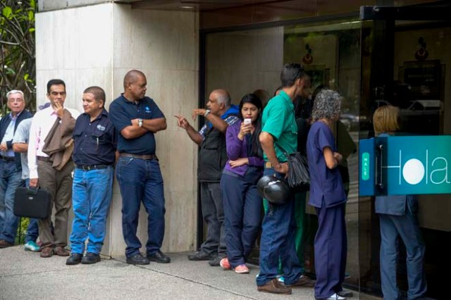 People queue to withdraw money from an automated teller machine (ATM) in Caracas on December 1, 2016. Venezuelan banks guaranteed their continued operation, after rumors about a close in December to adjust to an alleged issuance of bills of higher denomination. At the moment, the note of highest denomination is the one of 100 bolivars, that is just enough to buy a sweet. / AFP PHOTO / Federico PARRA