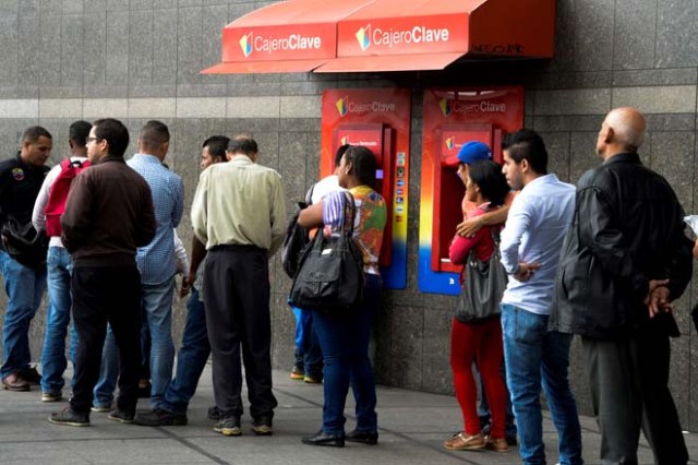 People queue to withdraw money from an automated teller machine (ATM) in Caracas on December 1, 2016. Venezuelan banks guaranteed their continued operation, after rumors about a close in December to adjust to an alleged issuance of bills of higher denomination. At the moment, the note of highest denomination is the one of 100 bolivars, that is just enough to buy a sweet. / AFP PHOTO / Federico PARRA