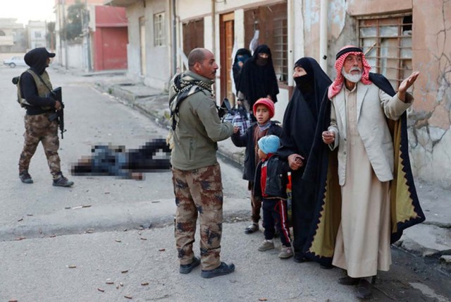 Un grupo de personas intenta escapar de Mosul frente al cuerpo sin vida de un combatiente del Estado Islámico.