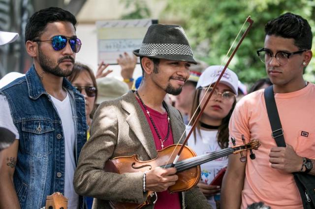 El violinista Wuilly Arteaga (c), un músico que ganó popularidad en el país luego de que su instrumento terminara dañado en medio de una protesta opositora que se tornó violenta, se presenta junto a otros músicos frente a un centenar de personas hoy, domingo 4 de junio de 2017, en la Plaza Brión de Chacaíto, en Caracas (Venezuela). Decenas de venezolanos se manifestaron en Caracas a favor de la paz y en contra del Gobierno de Nicolás Maduro, mientras la coalición opositora Mesa de la Unidad Democrática (MUD) llamó a sus simpatizantes a participar mañana en un "plantón" en varias vías del país. EFE/MIGUEL GUTIÉRREZ