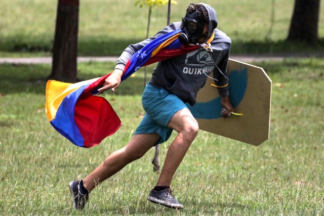 CAR29. CARACAS (VENEZUELA), 24/06/2017.- Un hombre que usa máscara de gas y lleva colgada una bandera venezolana corre durante una manifestación denominada "Venezuela le da un mensaje a la FAN (Fuerza Armada)" hoy, sábado 24 de junio de 2017, en Caracas (Venezuela). La oposición venezolana se moviliza hoy hasta las bases militares en Caracas y varios estados del país, mientras el chavismo marcha para conmemorar los 196 años de la Batalla de Carabobo, una acción militar decisiva en la independencia del país caribeño, y por el Día del Ejército Bolivariano. EFE/Miguel Gutiérrez