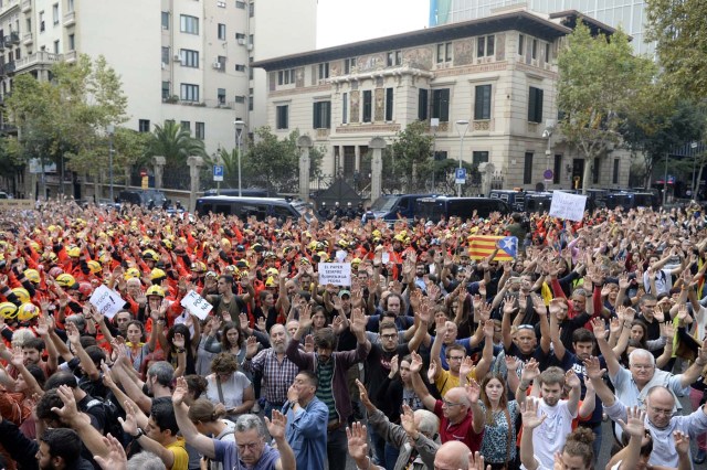 Protesters joined by firefighters raise their hands as they gather during a general strike in Barcelona called by Catalan unions on October 3, 2017. Large numbers of Catalans are expected to observe a general strike today to condemn police violence at a banned weekend referendum on independence, as Madrid comes under growing international pressure to resolve its worst political crisis in decades. / AFP PHOTO / Josep LAGO