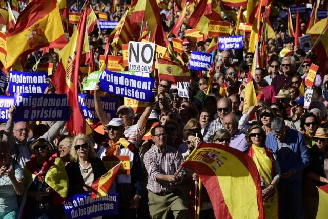 La gente sostiene carteles que dicen "No a la impunidad de golpistas" y "(presidente regional catalán Carles) Puigdemont a prisión" mientras agita banderas españolas durante una manifestación llamando a la unidad en Plaza de Colón en Madrid el 28 de octubre de 2017, un día después se impuso el control directo sobre Cataluña en un intento por separarse de España. España se movió para afirmar el dominio directo sobre Cataluña, reemplazando a sus funcionarios ejecutivos y altos para sofocar un impulso de independencia que ha sumido al país en una crisis y ha puesto nerviosa a la Europa secesionista. / AFP PHOTO / JAVIER SORIANO