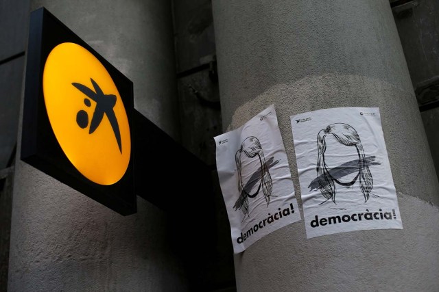 Caixa Bank's logo is seen next to banners reading "Democracy!", the day of a protest against the transfer of the bank's headquarters out of Barcelona, Spain, October 20, 2017. REUTERS/Ivan Alvarado