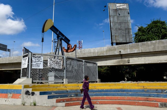 A woman walks by a small square with an oil pump in one of the access roads to the Central University of Venezuela, in Caracas on November 14, 2017. Venezuela has been declared in "selective default" by Standard and Poor's after failing to make interest payments on bond issues as it tries to refinance its $150 billion foreign debt. / AFP PHOTO / Federico PARRA