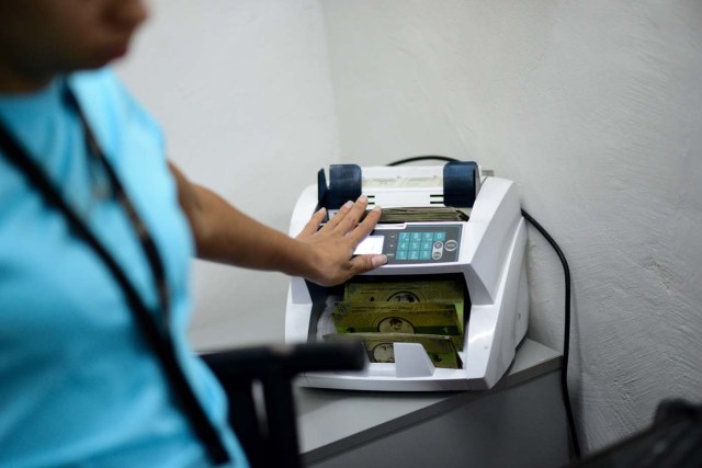 A cashier in the BanPanal communal bank explains the exchange value of the new local community currency, the panal, launched in the "23 de Enero" working-class neighbourhood in Caracas on December 15, 2017. A collective in a hilltop shantytown in Caracas created its own currency, the panal, in an attempt to fight chronic shortages of cash in inflation-ridden Venezuela. The currency can be exchanged locally for staples like sugar, rice (produced in the neighborhood itself), and bread. / AFP PHOTO / FEDERICO PARRA