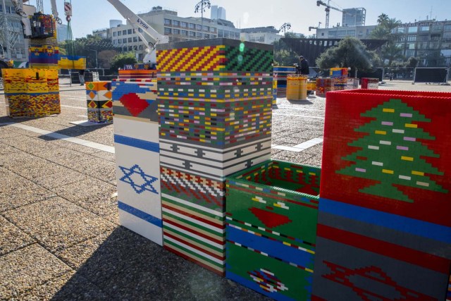 Workers and volunteers help assemble bricks during the construction of a LEGO tower in Tel Aviv's Rabin Square on December 26, 2017, as the city attempts to break Guinness world record of the highest such structure. / AFP PHOTO / JACK GUEZ