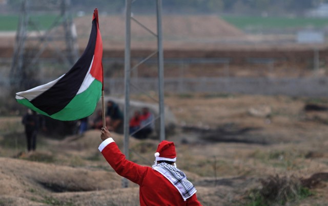 EST01. FRANJA DE GAZA, 19/12/2013.- Fotografía de un manifestante palestino vestido como Santa Claus y ondeando una bandera Palestina durante protestas contra la decisión del presiente de EE.UU. Donald Trump de reconocer a Jerusalén como capital de Israel hoy, martes 19 de diciembre de 2017, cerca a la frontera con Israel en la Franja de Gaza. EFE/MOHAMMED SABER