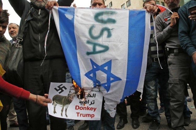 Palestinian demonstrators burn an Israeli flag and a poster depicting US President Donald Trump during a protest prior to clashes with Israeli security forces near a checkpoint in the city centre of the West Bank town of Hebron on December 20, 2017. / AFP PHOTO / HAZEM BADER