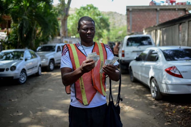 A car guard counts bills in the village of Chichiriviche de la Costa, some 70 km northwest of Caracas on January 13, 2018. The inhabitants of the village of Chichiriviche de la Costa, which depends on tourism, have come up with an ingenious way to deal with the lack of cash and internet connection. / AFP PHOTO / FEDERICO PARRA