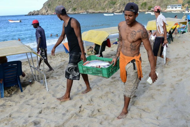 Fishermen carry fish at the beach in Chichiriviche de la Costa, a village some 70 km northwest of Caracas, on January 13, 2018. The inhabitants of the village of Chichiriviche de la Costa, which depends on tourism, have come up with an ingenious way to deal with the lack of cash and internet connection. / AFP PHOTO / FEDERICO PARRA