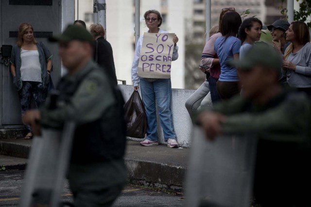 CAR14. CARACAS (VENEZUELA), 17/01/2018.- Una mujer sostiene un cartel en el que se lee "Yo soy Óscar Pérez" frente a miembros de la Guardia Nacional Bolivariana y la Policía Nacional Bolivariana que custodian las inmediaciones de la morgue en donde está cuerpo del exagente Pérez hoy, miércoles 17 de enero de 2018, en Caracas (Venezuela). Decenas de agentes de la Policía Nacional Bolivariana custodian desde la mañana de hoy los alrededores de la principal morgue de Caracas, después de que familiares de Óscar Pérez, el exagente alzado contra el Gobierno chavista quien falleció el lunes, exigieran identificar su cuerpo. EFE/MIGUEL GUTIÉRREZ