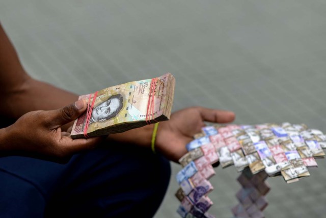 Wilmer Rojas, 25, holds a wad of Bolivar bills, which he uses to make crafts in Caracas on January 30, 2018. A young Venezuelan tries to make a living out of devalued Bolivar banknotes by making crafts with them. / AFP PHOTO / FEDERICO PARRA