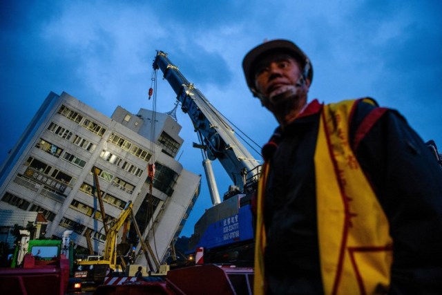 Un trabajador de rescate pasa junto a una grúa mientras el edificio Yun Tsui (atrás) se inclina hacia un lado después de un terremoto durante la noche en la ciudad taiwanesa de Hualien el 7 de febrero de 2018. / AFP PHOTO / Anthony WALLACE